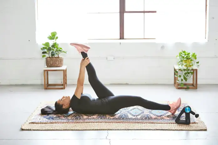 A woman lying on a mat and holding one leg raised during a stretch.